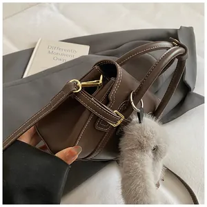 Detail of dark brown leather handbag with contrast stitching and plush animal charm