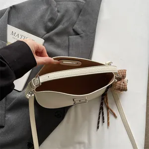 Détail du sac demi-lune en cuir crème avec fermoir métallique et breloque peluche