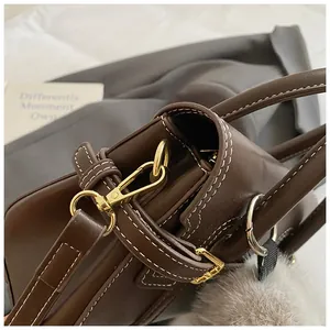 Detail of dark brown faux leather bag with white stitching, gold hardware and pompom