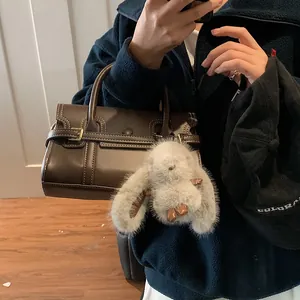 Close-up of a vintage dark brown leather handbag featuring a cute grey plush bunny charm