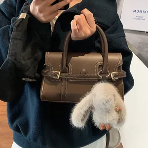 Detail of vintage brown handbag with white stitching, gold hardware and plush bunny charm