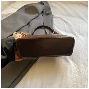 Détail du sac à bandoulière en similicuir marron foncé avec texture crocodile et petit pendentif