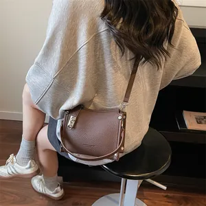 Brown lychee grain leather crossbody bag with silver buckle worn by a model in grey