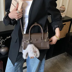 Close-up of brown leather handbag with contrast stitching and plush rabbit charm detail