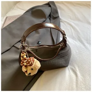 Détail du sac sous le bras marron à motif croco avec ours en peluche et breloque
