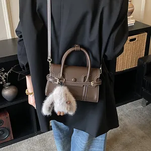 Detail of dark brown leather handbag with plush rabbit pendant and metal buckle closure