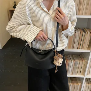 Gros plan d'un sac à main noir en cuir grainé avec fermoir rotatif et breloque ours