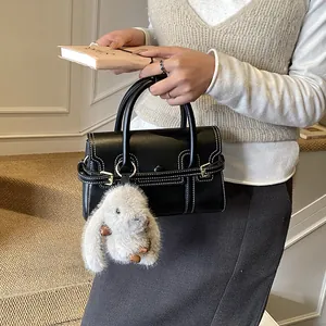 Detail of black faux leather handbag with white contrast stitching and bunny pendant