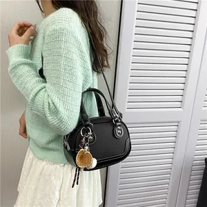 Detailaufnahme der schwarzen Ledertasche mit Kontrastnaht und Baseball-Anhänger
