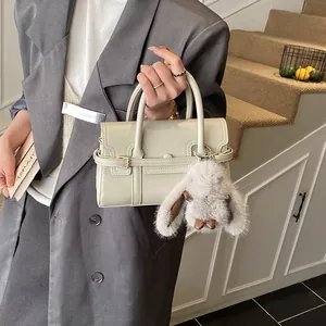 Detail of a beige handbag with a plush bunny charm and decorative strap accents