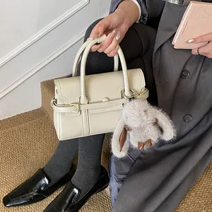 Detail view of a cream vintage handbag featuring a grey furry bunny charm on a grey coat