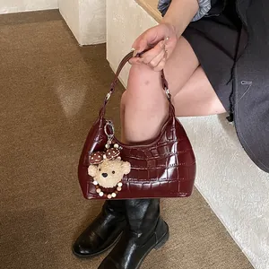 Détail du sac sous le bras bordeaux à motif crocodile avec un joli pendentif ours