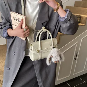 Close-up of a beige faux leather handbag with a plush rabbit charm for office commuting