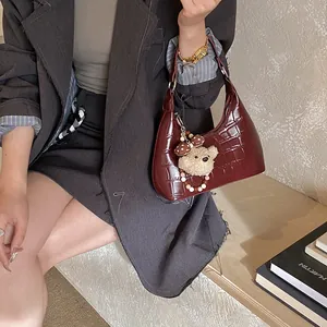 Détail du sac hobo croissant rouge foncé à motif crocodile avec un ours en peluche