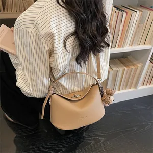 Détail du sac à main en cuir grainé abricot avec breloque d'ours porté à l'épaule du mannequin