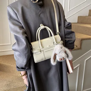 Close-up of beige leather crossbody bag featuring a cute grey plush bunny charm detail