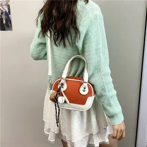 Detail der orange-weißen Bowling-Tasche mit Baseball-Anhängern auf mintgrünem Pullover