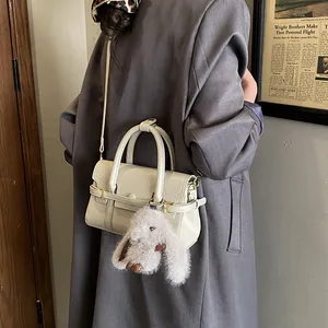 Detail of cream shoulder bag with plush rabbit charm against vintage backdrop
