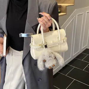 Detail of off-white faux leather handbag featuring a grey plush rabbit charm and metal clasp
