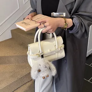 Close-up of white leather handbag featuring gold buckle detail and plush rabbit charm