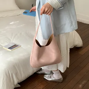 Dettaglio di una borsa hobo in pelle rosa tenuta da una modella in una stanza minimalista