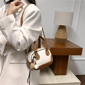 Detail der weißen Boston-Tasche aus Leder mit Baseball-Anhänger an Model in weißem Blazer