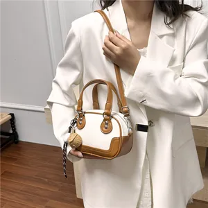 Detailansicht einer zweifarbigen Bowling-Tasche mit Erdbeer-Anhänger am weißen Blazer