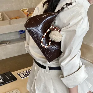 Détail du sac bandoulière marron foncé à motif crocodile avec chaîne et breloque ours