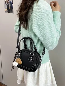 Schwarze Leder-Boston-Tasche mit weißen Nähten und Baseball-Anhänger am Modell