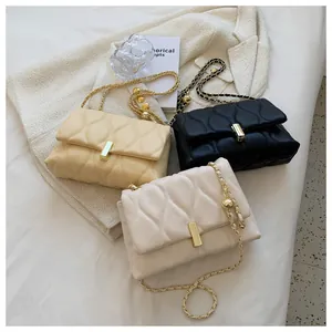 Detailed view of quilted crossbody bags in beige and black with gold chain and metal orb