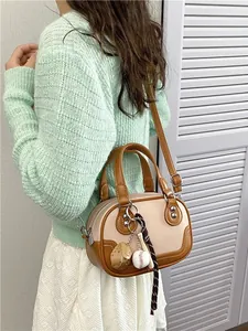 Schicke zweifarbige Boston Tasche mit Baseball-Anhänger und Gurt am Model gezeigt
