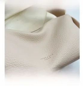 Detail shot of beige lychee texture leather with embossed brand logo on the bag