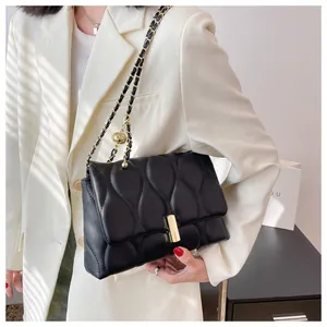 Detail of a black quilted leather crossbody bag with gold chain strap and wave pattern