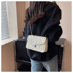 Detail of cream quilted crossbody bag featuring silver turn-lock and elegant chain strap