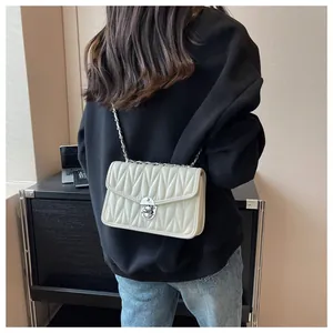 Close-up of beige quilted crossbody bag with silver chain strap worn on person
