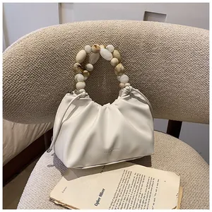 Close-up of white ruched cloud bag featuring marble-textured bead handle on a soft sofa