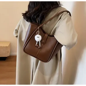 Detail of dark brown leather tote bag with vertical stitching and plush charm