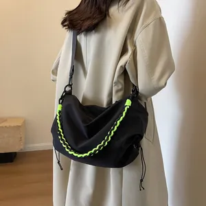 Minimalist black nylon crossbody bag with neon green woven cord and drawstring detail