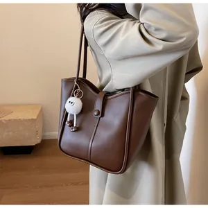 Detail of a large dark brown leather tote bag with stylish plush pendant and snap closure