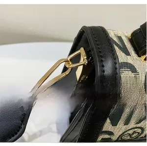 Close-up of golden metal hook on beige jacquard bag with black leather shoulder strap
