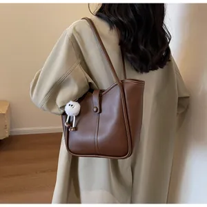 Detail of dark brown leather tote bag with white pompom charm shown on shoulder