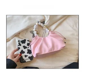 Pink pleated cloud bag with pearl handle shown next to a phone for size comparison