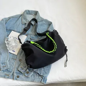 Minimalist black dumpling crossbody bag with vibrant green woven rope handle on denim