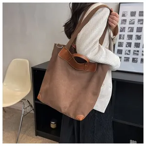 Detail of dark brown canvas tote bag with leather拼接 accents and wide shoulder strap