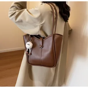 Close-up of brown leather tote bag with vertical stitching and plush charm accessory