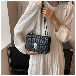 Detail of quilted black shoulder bag with silver chain strap on a white pleated dress