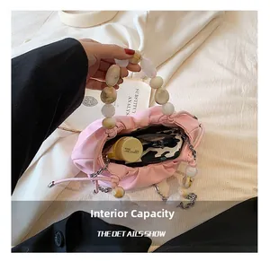 Internal capacity of light pink pleated handbag showing cosmetics and marble bead handle