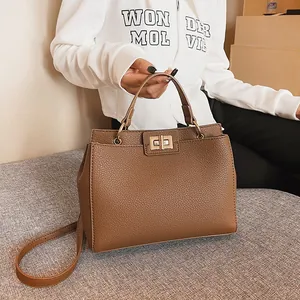 Detail of a brown leather handbag with a golden rotating lock on a grey sofa