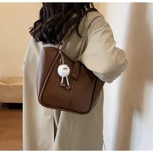 Detail view of deep brown leather tote bag with monster plush charm on shoulder of model