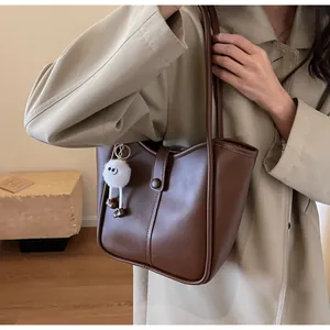 Close-up of brown leather tote bag with a white plush monster charm on a stylish model